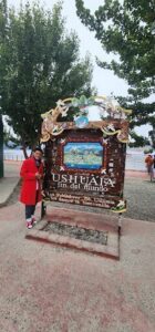 A man in a red jacket stands in front of a sign for Ushuaia.