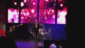 A man in a suit is singing on stage while a band plays behind him.