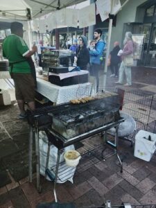 A man is cooking food on a grill, while a woman and a child watch.
