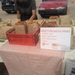 A man is smiling at the camera while standing in front of a table filled with food.