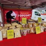 A man is standing in front of a table filled with bags of popcorn.