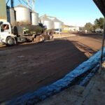 A man is standing next to a large truck, which is parked on a dirt road.