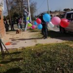 A man is standing on a ladder, holding balloons and preparing to release them.