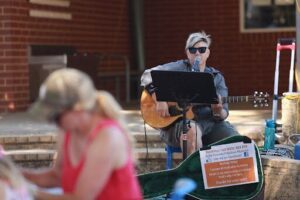 A man plays a guitar while a woman sits nearby.
