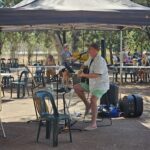 A man plays guitar under a tent, surrounded by chairs and people.