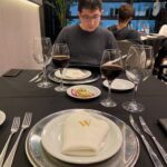 A man sits at a table with a plate of food and several wine glasses.