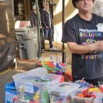 A man stands in front of a table filled with various items, including a collection of balloons.