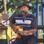 A man wearing a black hat and striped shirt is playing a guitar.
