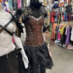 A mannequin wearing a corset and a black hat is displayed in a store.