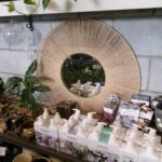 A mirror with a wicker frame sits on a shelf among other items.