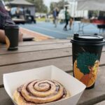 A person is enjoying a delicious pastry, which includes a cinnamon roll and a cup of coffee.