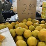 A person is holding a bag of lemons, and there is a sign that says 2.5 kilo for 2.50.