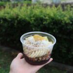 A person is holding a bowl of food, which includes bananas and other ingredients.