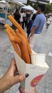 A person is holding a cup of churros with a small cup of sauce.