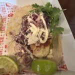 A plate of food with a taco, sour cream, and vegetables.