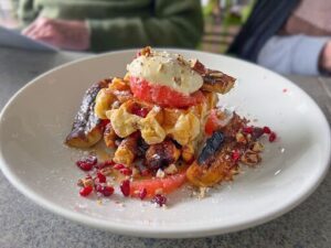 A plate of food with a variety of items on it, including a waffle, fruit, and nuts.