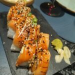 A plate of sushi with rice, seaweed, and fish on a black plate.