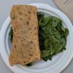 A sandwich with greens and a wrap on a plate.