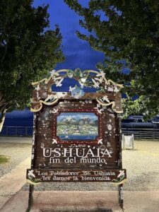 A sign for the town of Ushuaia is displayed in front of a tree.