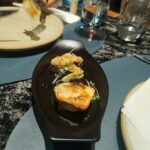 A small, delicious-looking pastry is served on a plate, accompanied by a fork and a wine glass.