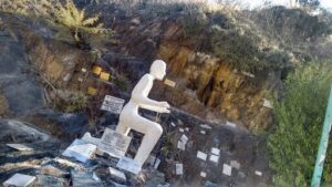 A statue of a man sitting on a rock is surrounded by many headstones.
