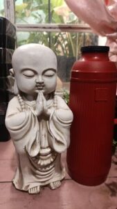 A statue of a person praying is next to a red bottle.
