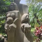 A statue of a woman and two children is displayed in a garden.