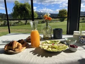 A table full of food and drinks, including a bowl of fruit, a vase of flowers, and a pitcher of orange juice.