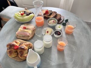 A table full of food and drinks, including a pitcher of orange juice, a bowl of fruit, and a variety of sandwiches.