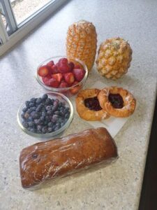 A table full of fruits and pastries, including a loaf of bread, a bowl of strawberries, and a pineapple.