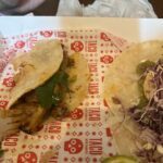 A taco with meat and vegetables on a paper plate.