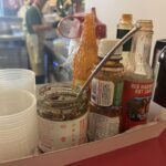 A variety of condiments and sauces are displayed in a tray, including a jar of salsa and a bottle of hot sauce.
