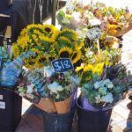 A variety of flowers are displayed in baskets, with prices labeled for each type.