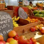 A variety of fruits and vegetables are displayed at a market, including bananas, apples, and oranges.