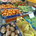 A variety of fruits and vegetables are displayed at a market, including pineapples, oranges, and tomatoes.