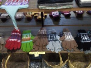 A variety of gloves are displayed on a shelf, including brown, green, and gray ones.