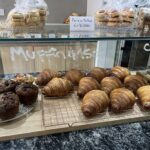 A variety of pastries, including croissants and muffins, are displayed on a counter.