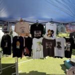 A variety of shirts are displayed under a tent, including a shirt with a picture of a cat.