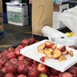 A white sign with the number 2 on it is placed in front of a pile of peaches.