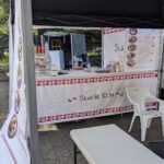 A white tent with a red and white tablecloth is set up for a food stand.