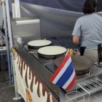 A woman is standing in front of a food cart, which has a flag on it.