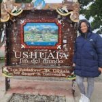 A woman standing in front of a sign that says "Ushuaia, fin del mundo".