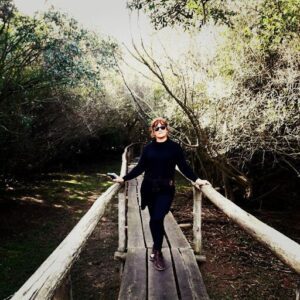A woman wearing sunglasses and a black shirt stands on a wooden bridge.
