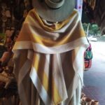 A yellow and white striped blanket hangs on a wall, with a cowboy hat placed on top of it.