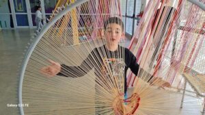 A young boy stands in front of a large ball of yarn, posing for a picture.