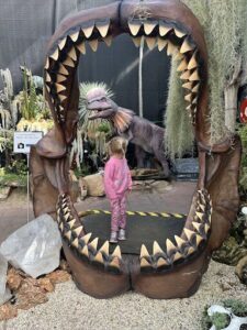A young girl stands in front of a large shark's mouth, seemingly unafraid.