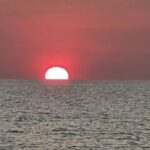 The sun sets over the ocean, casting a warm glow on the water.