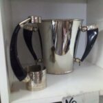 Two silver pitchers sit on a shelf, one next to the other.