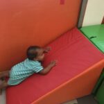 A baby crawls up a red cushion.