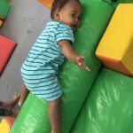 A baby is laying on a green and yellow mat, reaching out with his hand.
